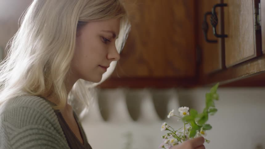 A woman places small flowers together in an arrangement standing in her kitchen
