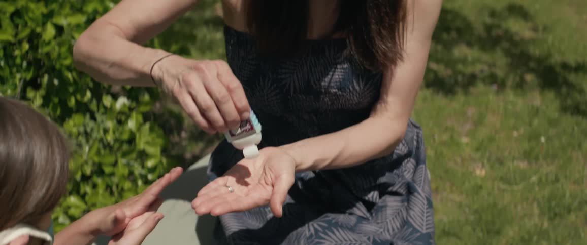 Mother and daughter sitting on the grass use a hand sanitizer as a precaution due to coronavirus