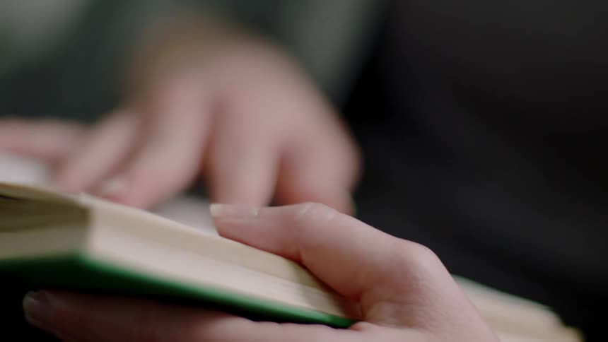 A womans hands holding and turning a page in a green book