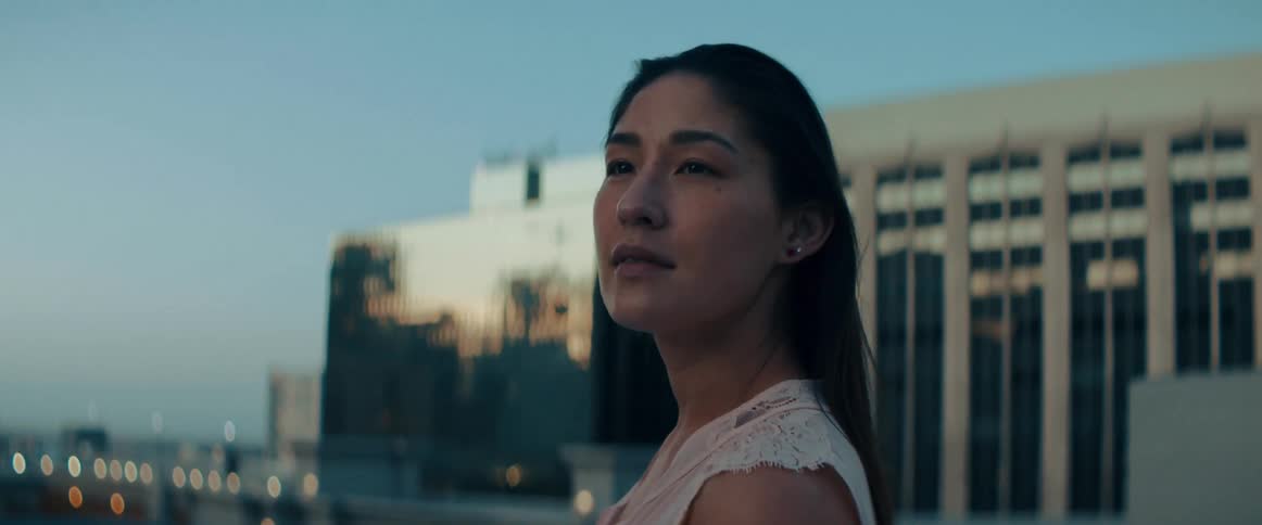 A woman standing on a balcony looking out over a city in the evening