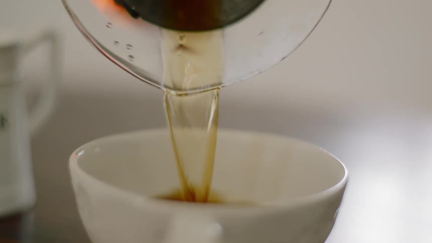 Coffee is poured into a white cup from a glass carafe and then the pot is placed back down