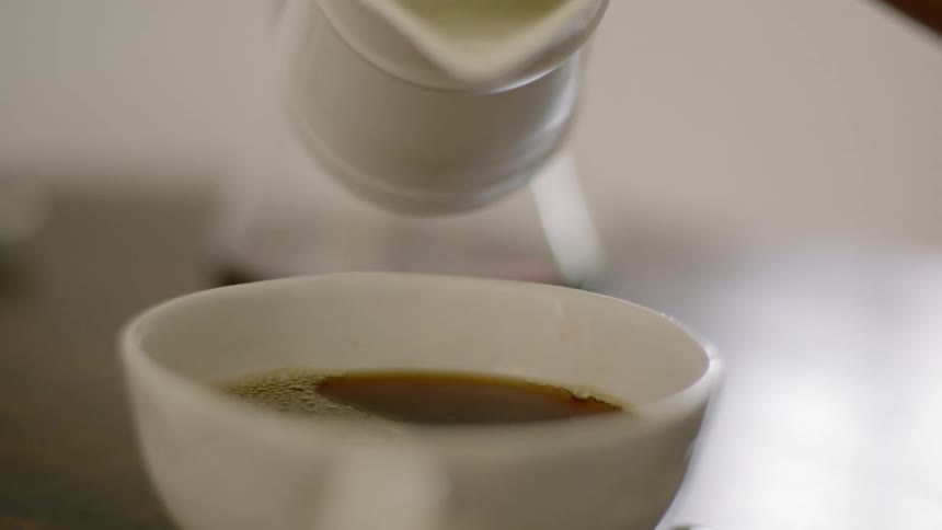 Woman adds some cream to the coffee in the kitchen