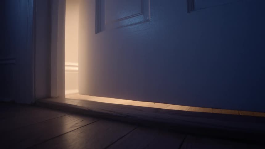 An interior door in a house is ajar and light shines on the other side