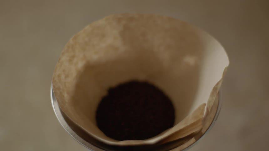 A person putting coffee grounds in a filter with a silver scoop