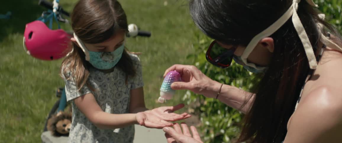 A mom put some hand sanitizer in her daughters hands and shows her how to rub them together while kneeling on the path next to her bicycle