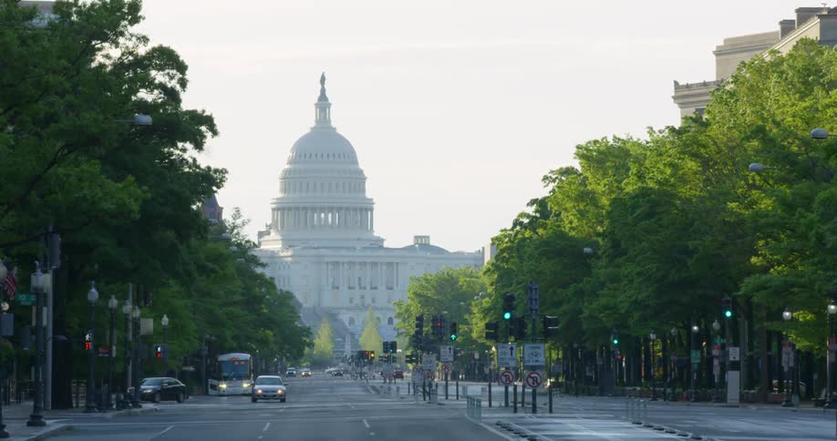A city street with vehicles and trees with the united states capitol building in the background
