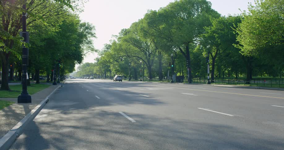 Vehicles drive on a wide highway next to the public park