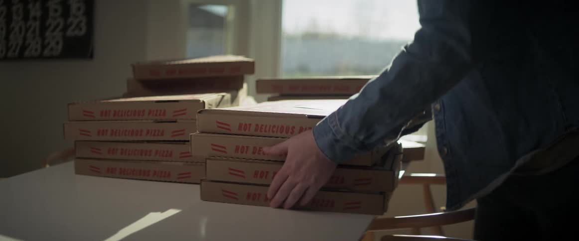 A person placing a note on top and grabbing four pizza boxes off of a table