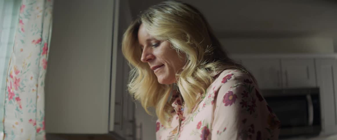 A blonde woman nervously washes dishes at her kitchen sink