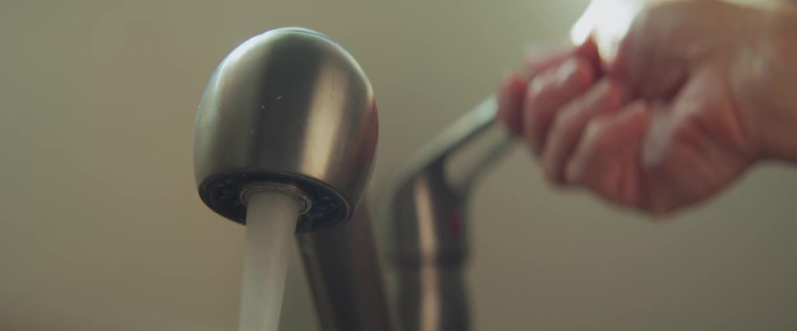 Someone turns on a stainless steel sink faucet