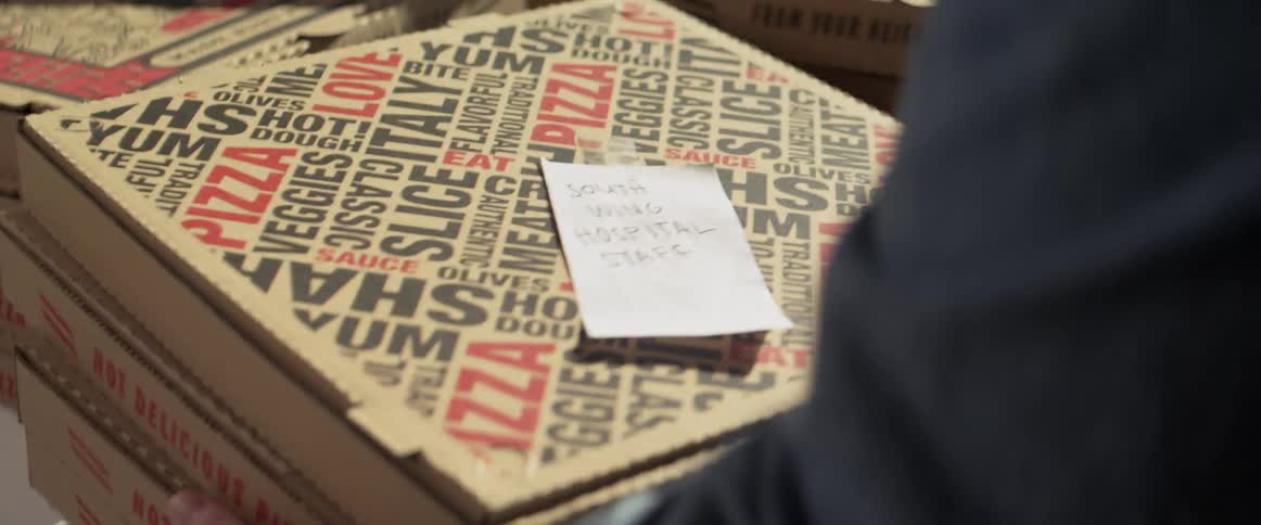 A persons hands placing a note on top of a pizza box then grabbing the pizza boxes off the table