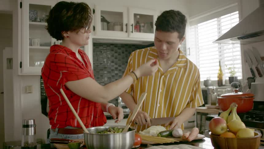 A teenage boy and girl are preparing a meal together in a home kitchen