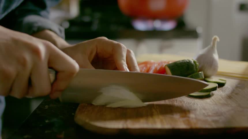 A person picks up a knife and chops onion on a wooden cutting board