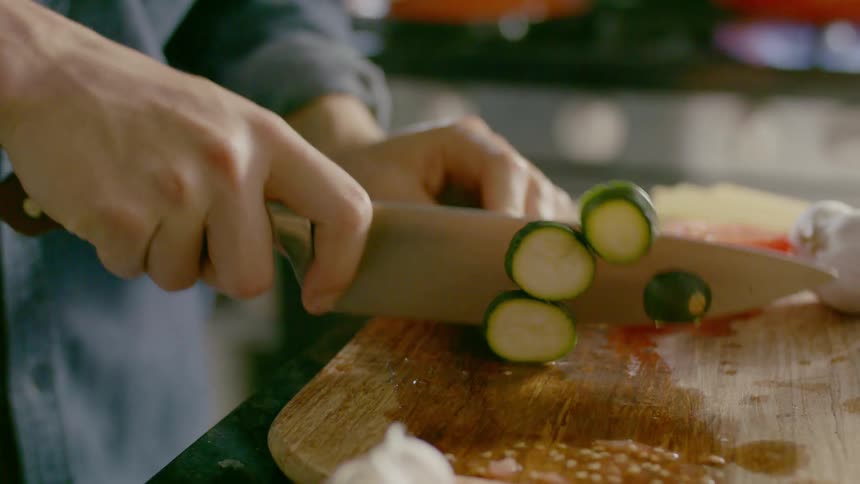 A person is cutting vegetables as pots cook on the stove