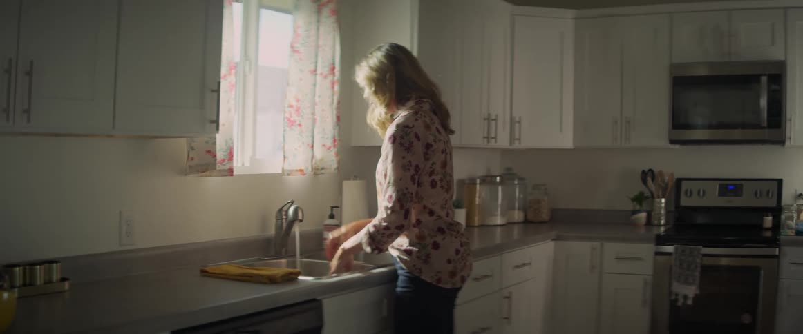 A woman washing her hands in a kitchen sink before drying them with a towel
