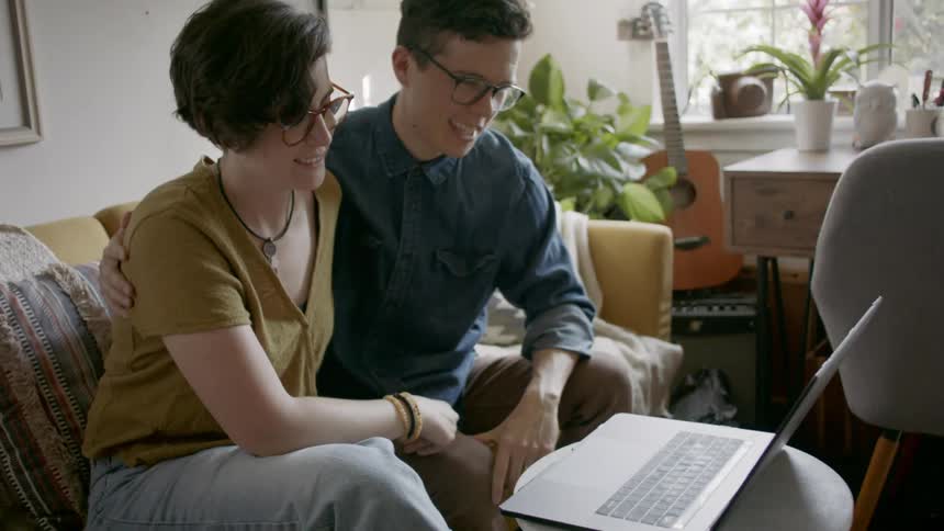A man and woman sit on a couch having a video call on a laptop