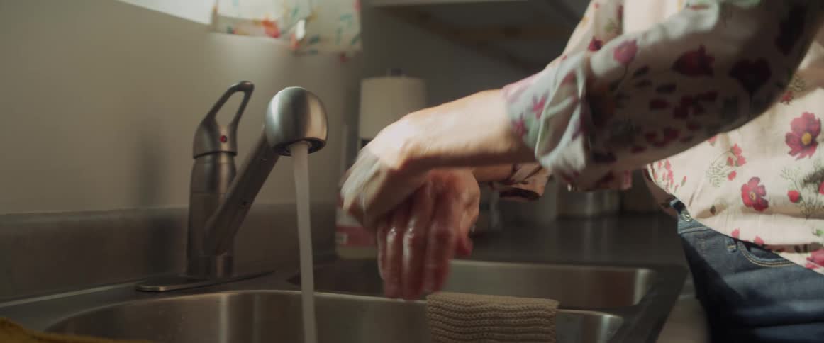 A woman washes her hands at her kitchen sink