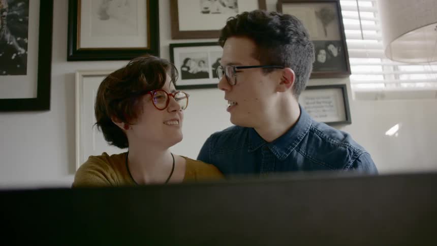 A boy sits close to a girl and has his arm around her and they talk and laugh
