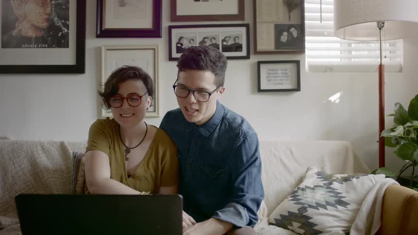 A man and woman sitting together on a sofa video chatting with a laptop