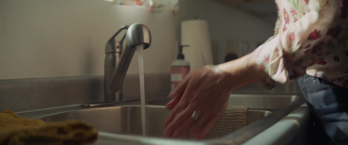 A womans hands turning on a water faucet and washing her hands with soap in a sink