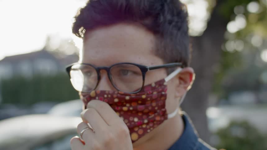 A young man putting on a patterned face mask will standing outdoors