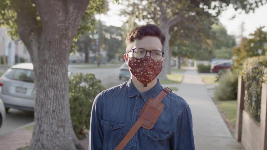 A teenager wearing a mask walks along a city street