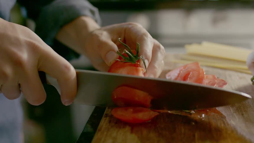 A person chopping a tomato on a wooden cutting board in a kitchen