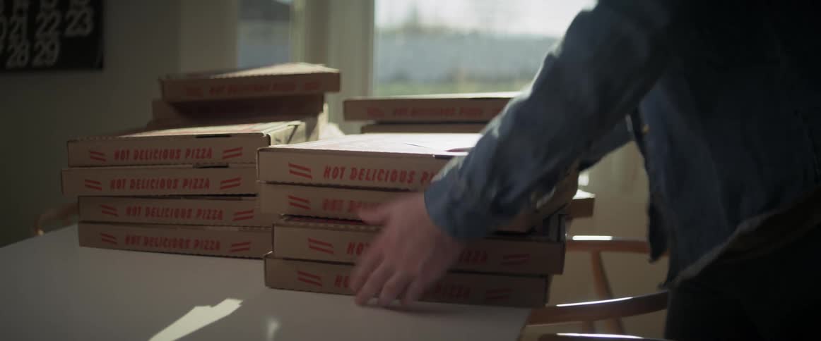 A person placing a note on top and grabbing four pizza boxes off a table