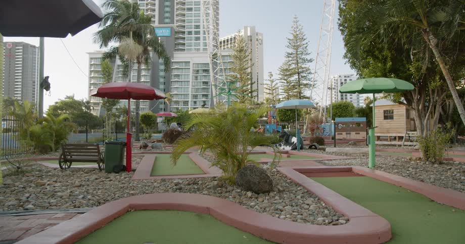 Palm fronds sway in breeze on putt putt golf course near skyscrapers