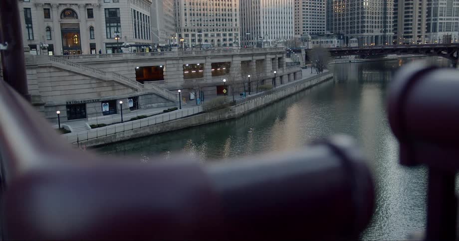 A bus turns onto a city street next to the river lined with buildings and walkways