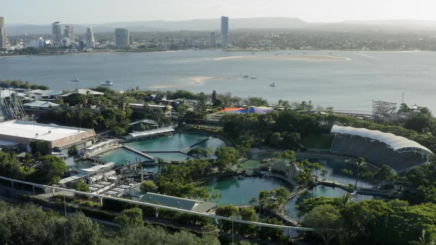 The empty stands and pools of a waterfront aquarium with boats in the harbor and city skyline behind