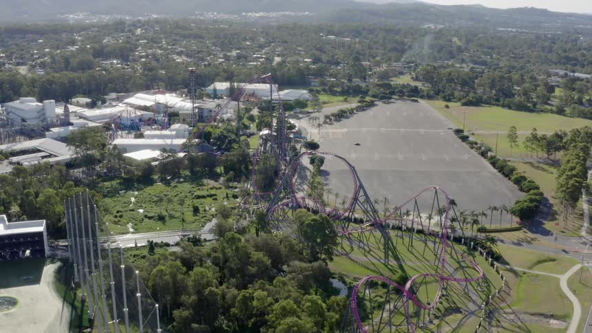 A roller coaster near a parking lot with buildings in the background