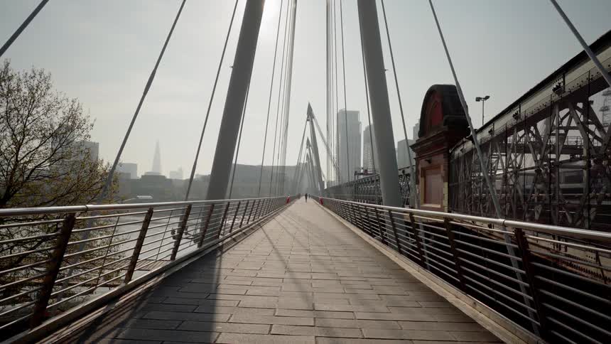 A person is walking along a city highway pedestrian bridge over a river