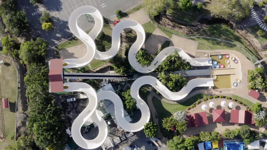 A water slide that is surrounded by trees next to a parking lot