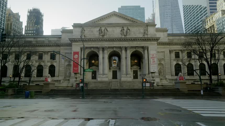 A museum with an empty city street in the foreground and buildings and skyscrapers in the background