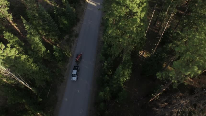 A truck with a trailer is traveling down a road in the woods