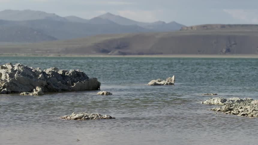 Water flows between shoreline rocks beside a river and mountains