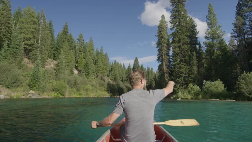 A man is sitting in a boat holding an ore on a sunny day