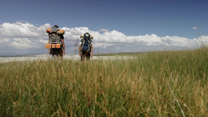 Hikers walk through a grassy field in the wilderness