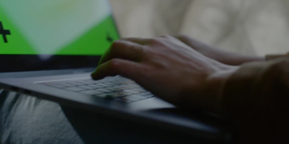 A person types on a laptop while laying on a couch