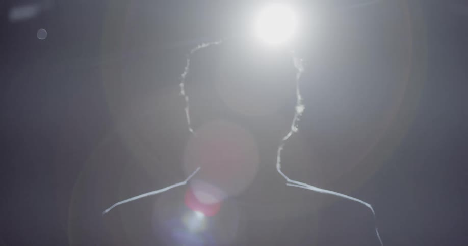 The silhouette of a man standing on a stage in a dark theater with a spotlight shining on him