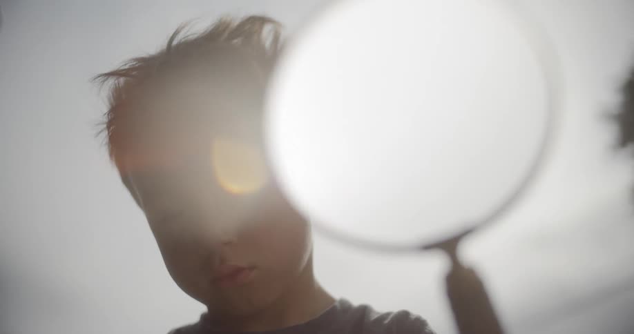 A boy gazing down at the ground while holding a large magnifying glass
