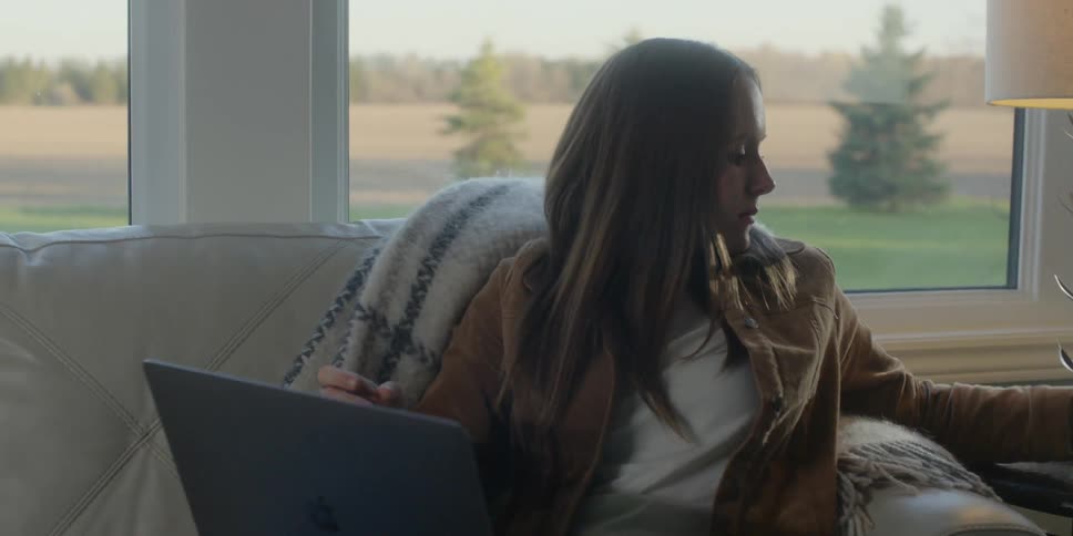 Woman sitting on the couch sips her coffee and uses a laptop in the living room at home