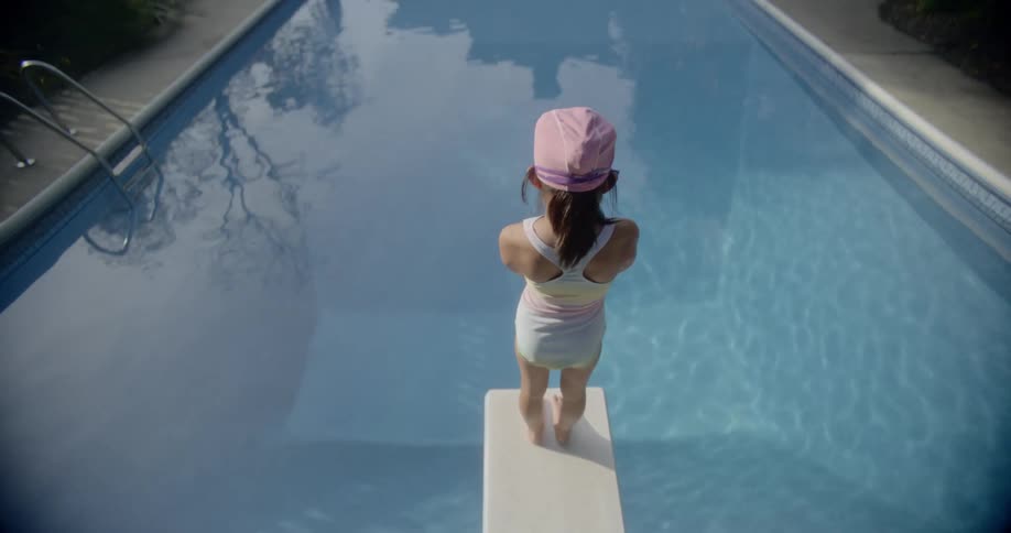 A child stands on a diving board next to a pool