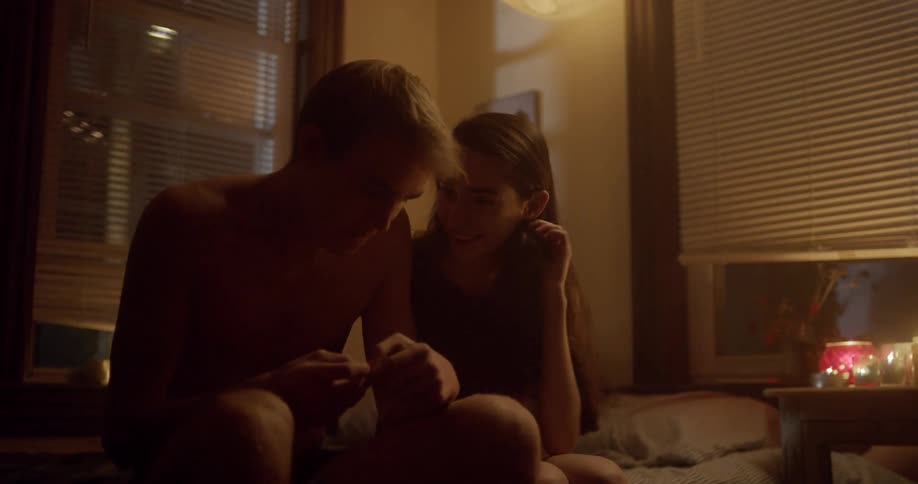 Teenage boyfriend and girlfriend sit and cuddle on a bed surrounded by candles