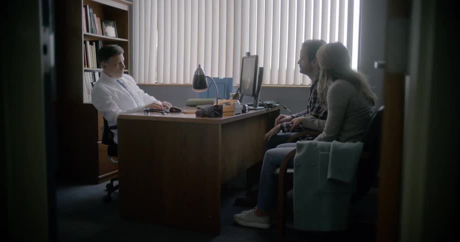 A doctor delivers news to a man and woman in his office
