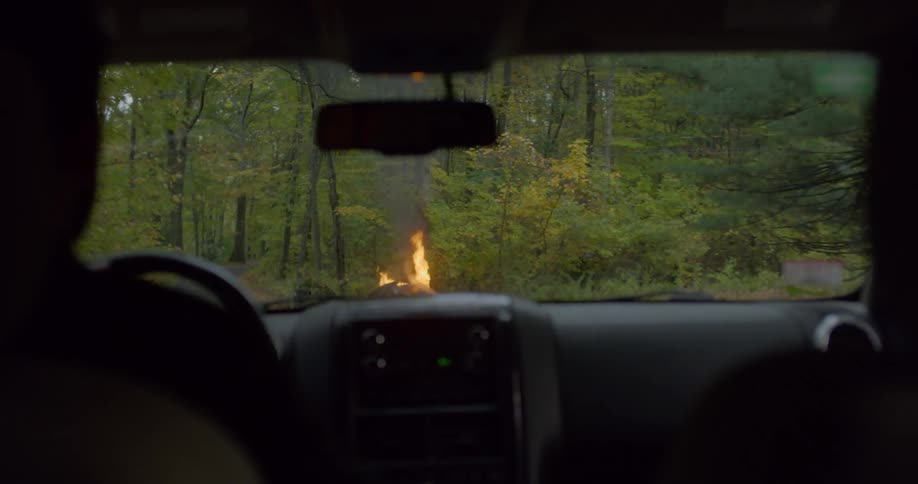 A person driving a vehicle in a remote road where they stop at a car on fire at the side of the road