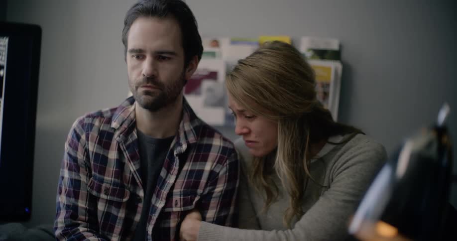 A woman cries and kisses her husbands shoulder as they receive bad news in a doctors office