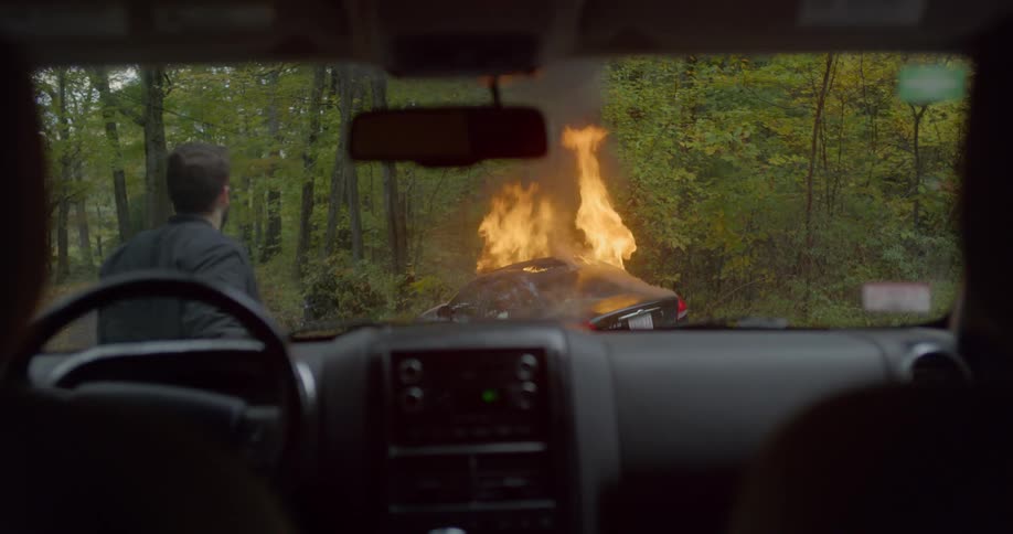 A man comes out of a vehicle and sees a car on fire