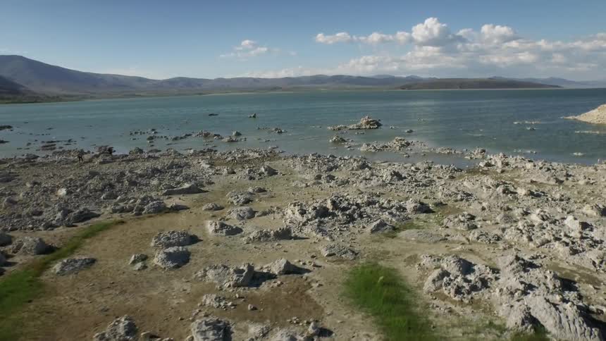 Rocks, sand and grass lead to lake surrounded by mountains